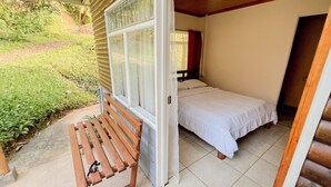 Een slaapkamer met een bed, een bankje buiten en uitzicht op groen.
