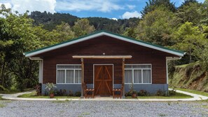 Una cabaña de madera con techo verde, dos ventanas y una puerta central.