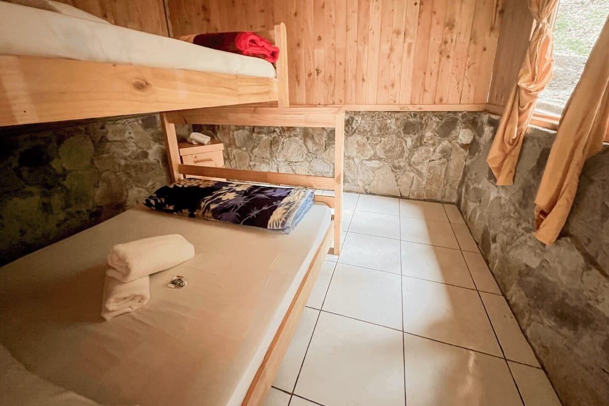 Une petite pièce rustique avec un lit superposé, un lit simple et un mur en pierre.