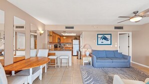 A modern living room with a blue sofa, a wooden dining table with chairs, a kitchen in the background, and a ceiling fan. - Manatee Harbor: Marina, Heated Pool-Spa, Island Ferry with PRIVATE Beach access! (Placida)