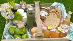 A wooden crate filled with food items, including bread, eggs, honey, and a bottle of pomegranate juice, placed on grass. - Bienvenue à la Ferme (Maresches)