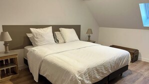 A bedroom with a large bed, two bedside tables with lamps, wooden flooring, and a sloped ceiling. - Bienvenue à la Ferme (Maresches)