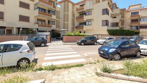 Un edificio residencial de varios pisos con balcones, un paso de peatones y automóviles estacionados.