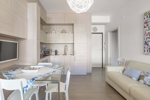 Une cuisine moderne avec des meubles blancs, une table à manger avec des chaises et un canapé dans l’espace salon.