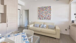 Una sala de estar moderna con un sofá beige, una mesa de centro de vidrio y un comedor con una mesa dispuesta para dos personas.