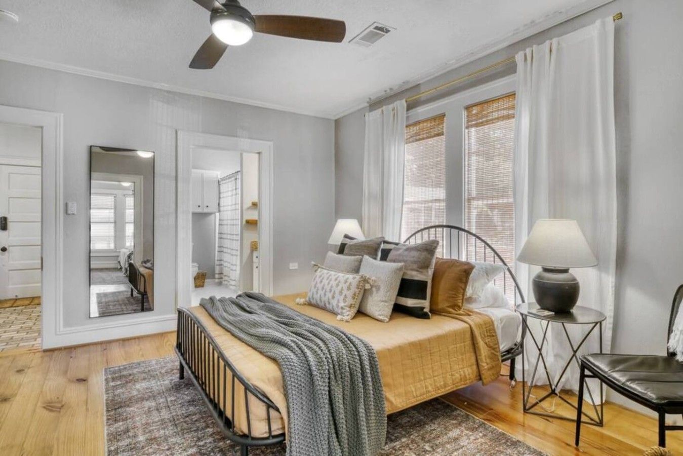 A bedroom with a bed, bedside tables, a ceiling fan, and a view of the outside through a window.