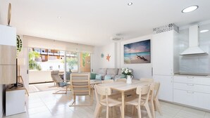 Una cocina moderna con armarios blancos, una mesa de comedor de madera y un amplio ventanal con vistas a edificios y vegetación.