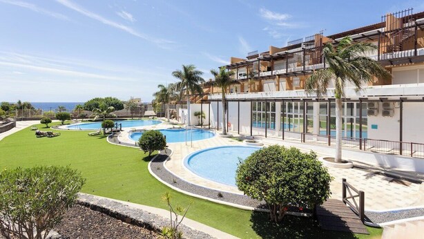 Un resort con varias piscinas, un césped bien cuidado y un edificio con balcones con vistas a las piscinas.