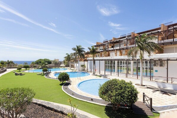 A resort with multiple swimming pools, a well-maintained lawn, and a building with balconies overlooking the pools.