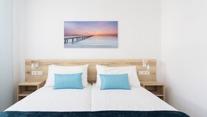 Habitación de hotel con una cama grande, dos mesitas de noche, un cabecero de madera y un cuadro colgado en la pared que muestra un atardecer sobre un muelle.