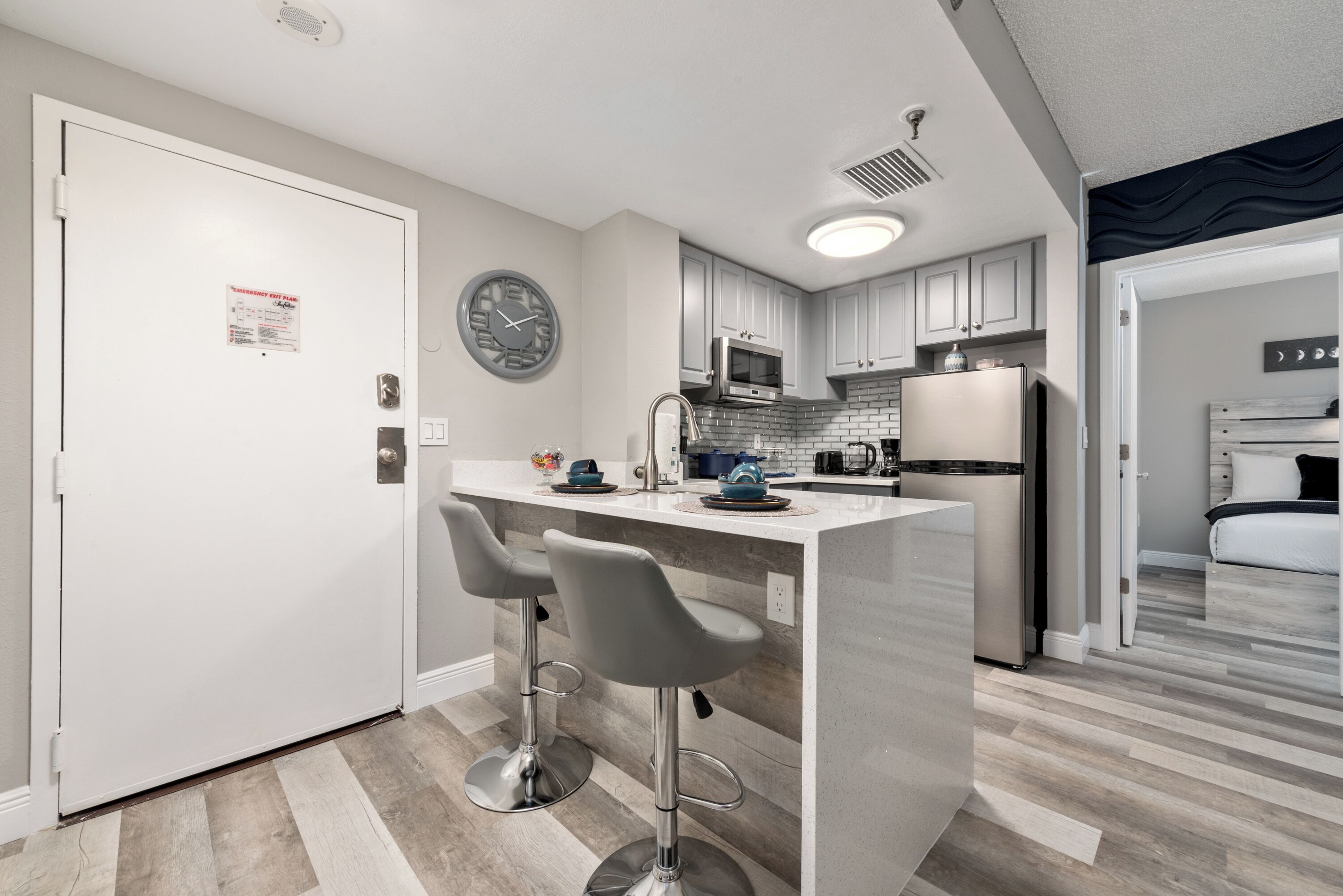 A modern kitchen with a central island, bar stools, stainless steel appliances, and a clock on the wall.