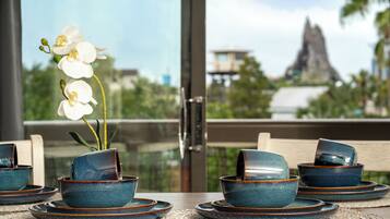 A dining table with blue ceramic bowls and plates, a vase with white flowers, and a view of a mountain through a glass door.