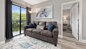 A modern living room with a brown leather sofa, a patterned throw pillow, and a large abstract painting on the wall. - Apartment next to International Dr and Universal (Orlando)