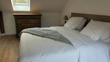 Une chambre à coucher comprenant un lit, une table de chevet, une lampe, une commode et une lucarne.