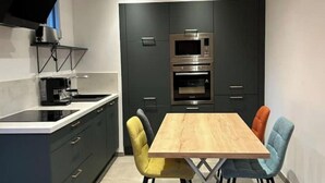 Cuina moderna amb armaris foscos, microones integrat i taula de dinar de fusta amb quatre cadires.