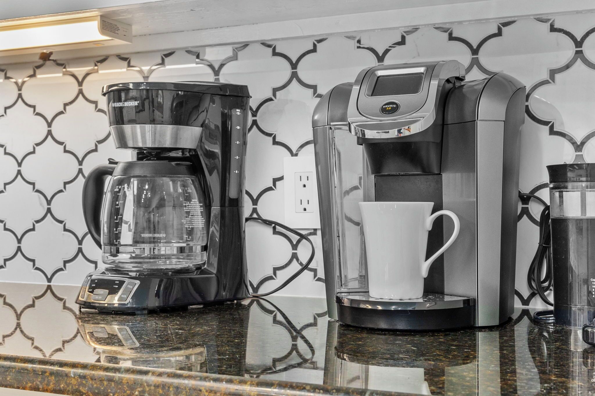 A coffee maker and a water dispenser on a kitchen counter with a patterned backsplash.
