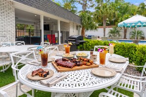 An outdoor dining area with a barbecue grill, a pool, and a covered seating area.