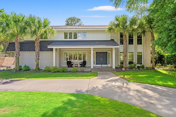 A two-story house with a front porch, palm trees, and a well-maintained lawn.