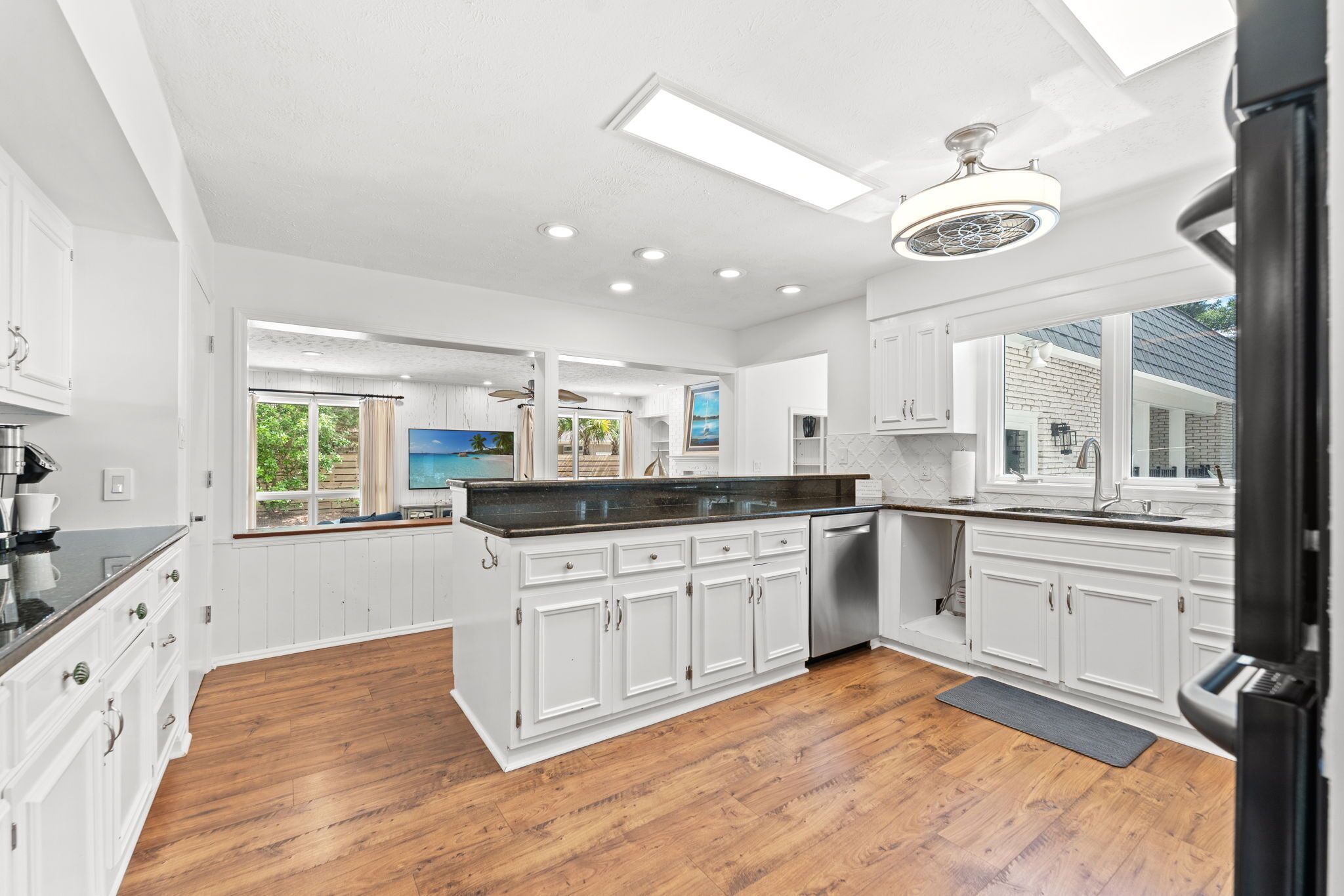 A modern kitchen with white cabinets, a black countertop, and a wooden floor.