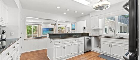 A modern kitchen with white cabinets, a black countertop, and a wooden floor.