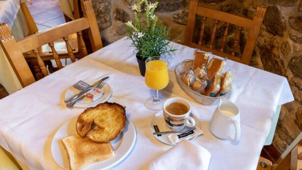 Una mesa de desayuno con tostadas, un vaso de zumo de naranja, una taza de café, un bol de pasteles y una pequeña planta en maceta.