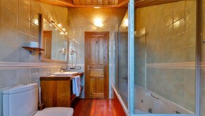 Un baño con suelo de madera, un inodoro, un lavabo, un espejo y una ducha con mampara de vidrio.