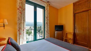 Una habitación de hotel con cama, televisión, armario de madera y balcón con vistas.