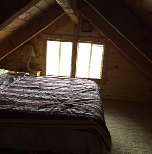 Cozy loft-style room with a large bed, two windows, and exposed wooden beams.