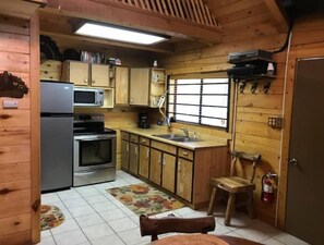 Kitchen equipped with a refrigerator, microwave, oven, and sink under a window.