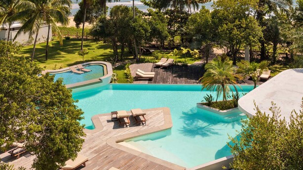 A resort pool with palm trees and a beach view. - Auka Boipeba (Cairu)