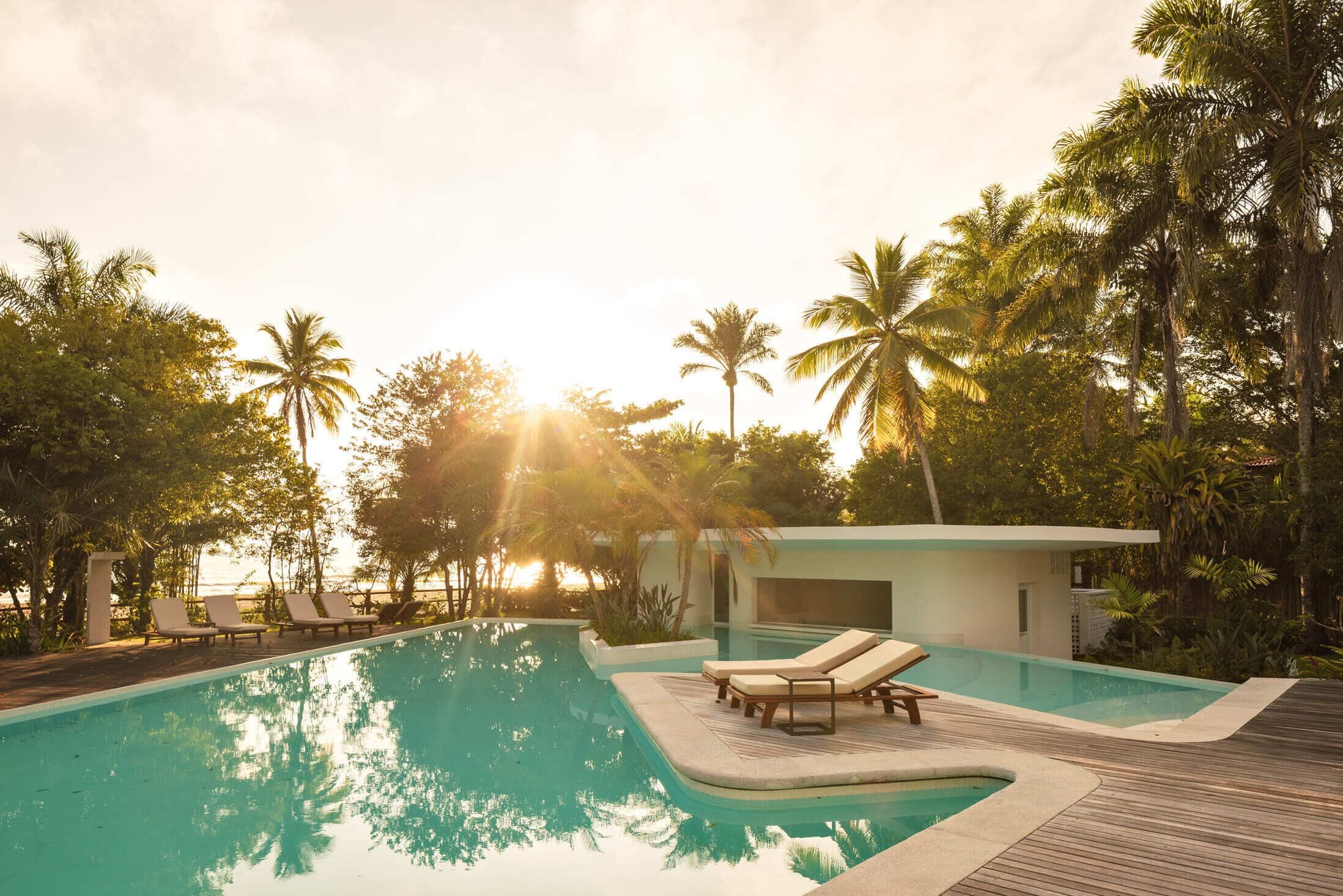 A pool with lounge chairs and a modern building surrounded by palm trees.