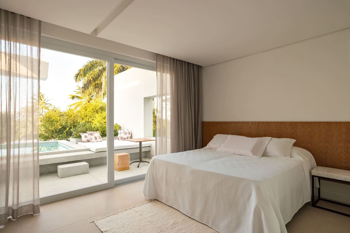 A bedroom with a large bed, a view of a pool and outdoor seating, and a sliding glass door to the outside.
