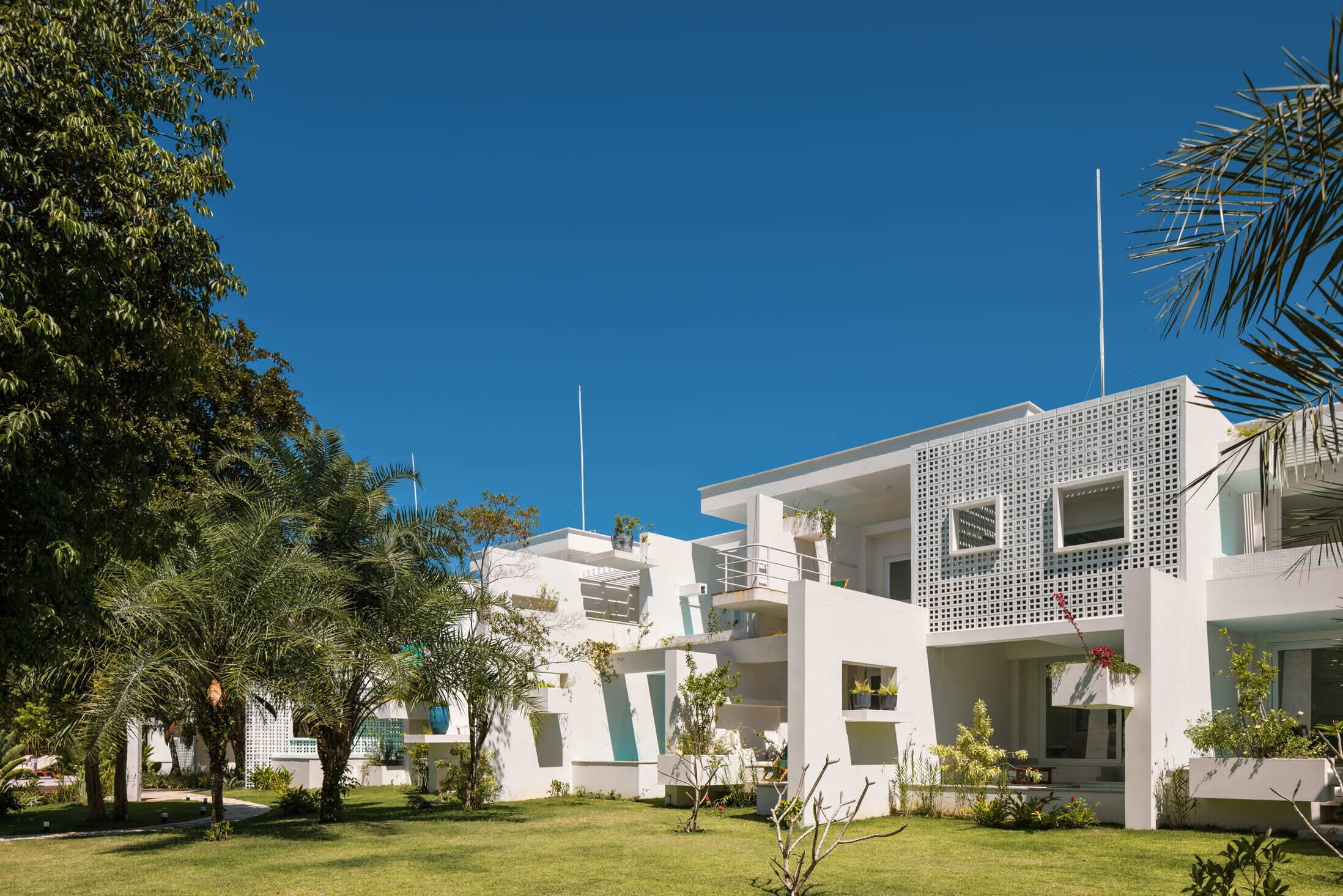 Un edificio moderno con varios balcones, rodeado de vegetación cuidada y un cielo azul despejado.