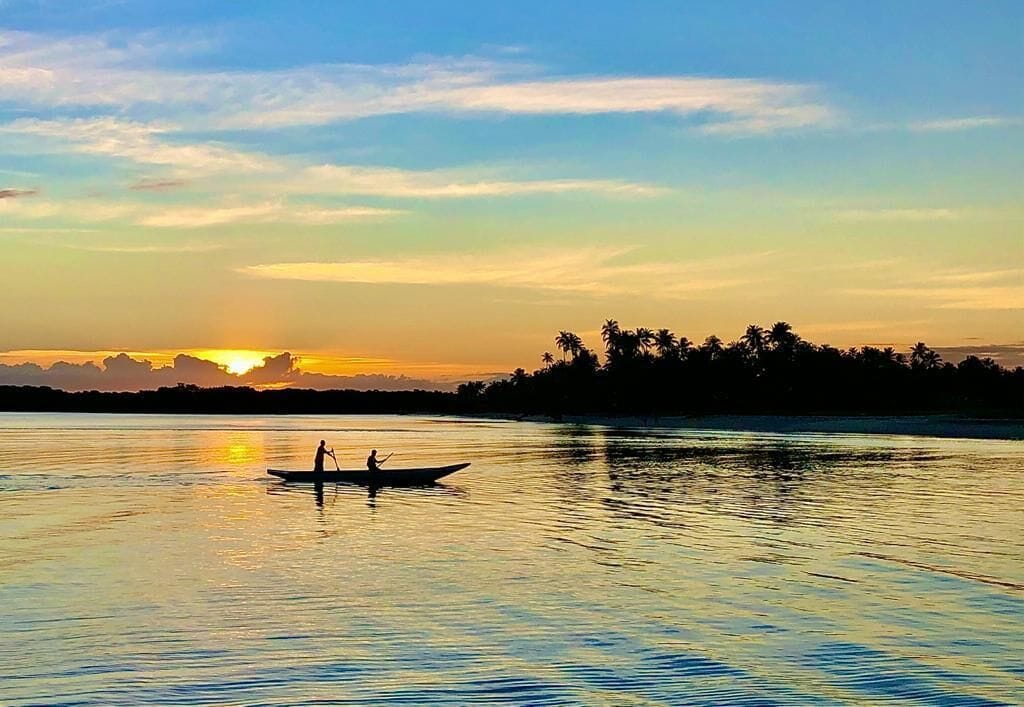 A calm river at sunset with a silhouette of a person paddling a boat.