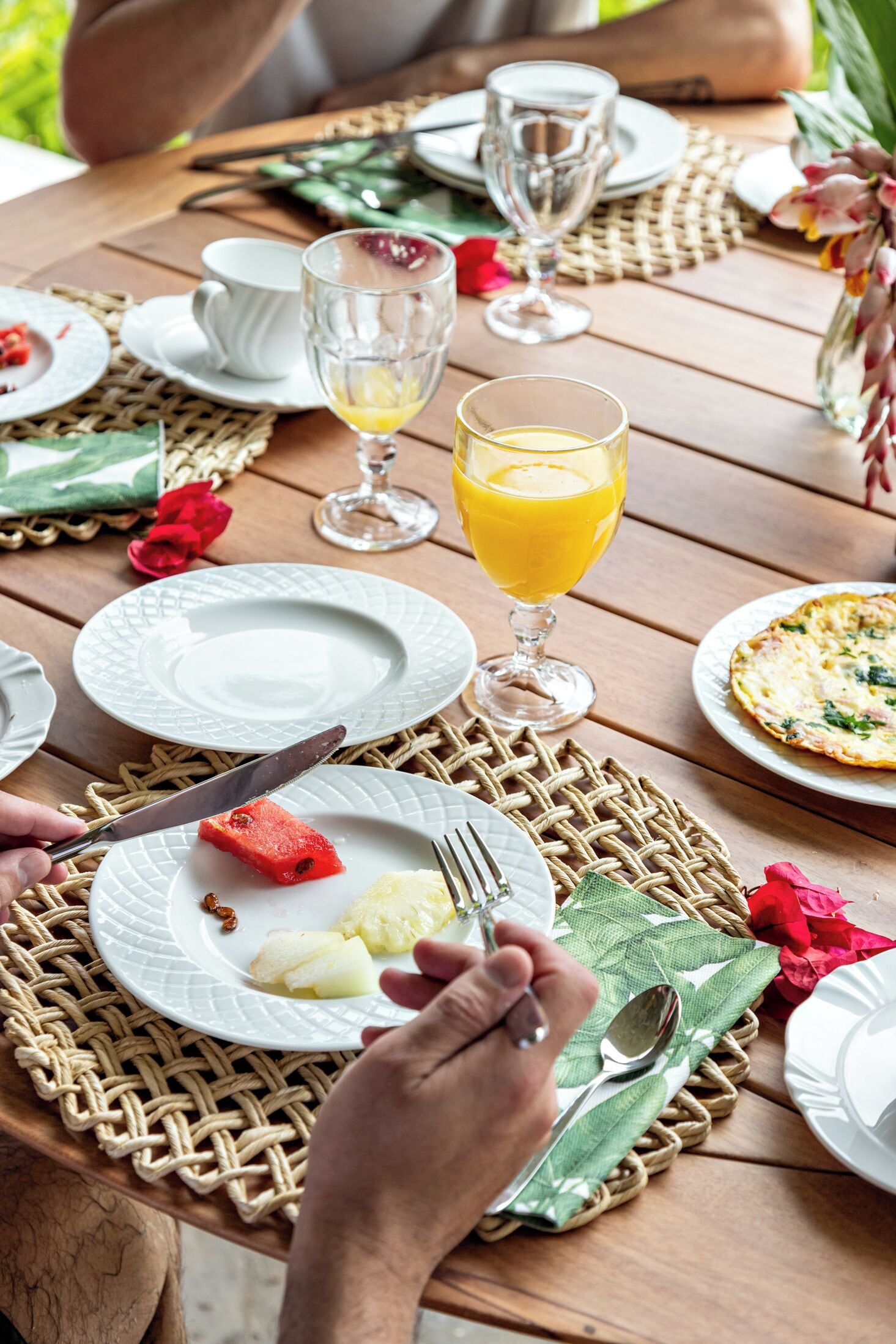 Una mesa de madera con platos, cubiertos y un vaso de jugo de naranja.