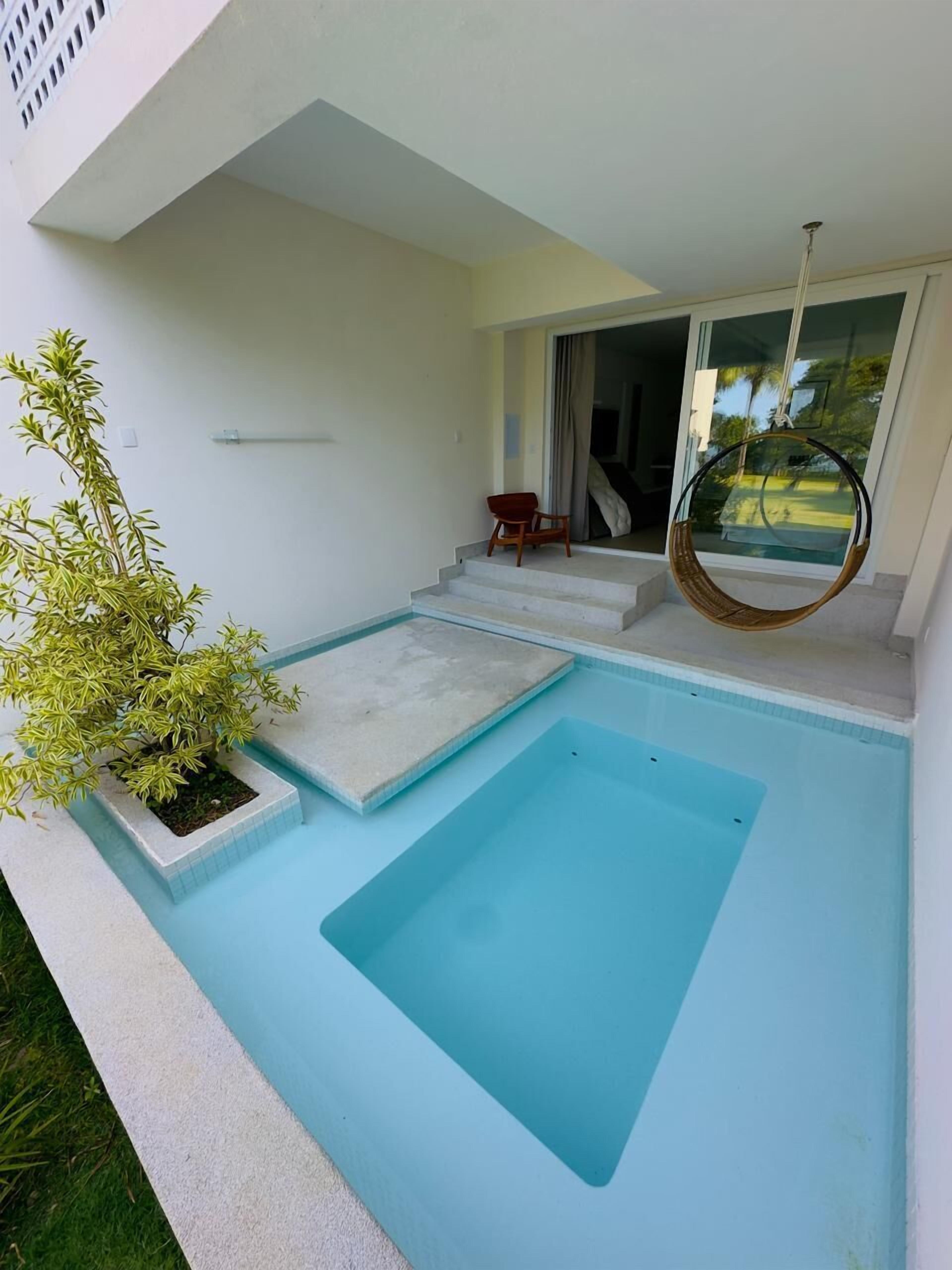 Un área de piscina moderna al aire libre con un espacio de descanso pequeño y una silla colgante.