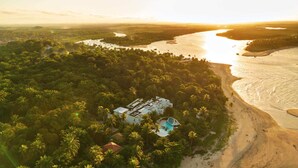 An aerial view of a coastal resort with a swimming pool, surrounded by dense tropical vegetation and a river. - Auka Boipeba (Cairu)