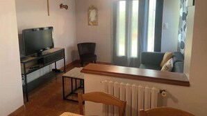 Ein Wohnzimmer mit Fernseher, Esstisch, Stühlen, Heizkörper und einem fenster mit Vorhängen.