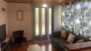 Ein Wohnzimmer mit Holzboden, einem schwarzen Sessel, einem grauen Sofa mit gemusterten Kissen und einem Fernsehschrank.
