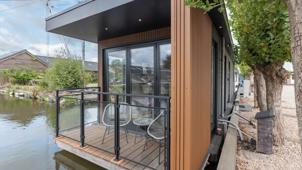 A modern floating structure with a wooden deck, glass windows, and metal railings. - Luxury Watervilla Near Amsterdam and Schiphol (Aalsmeer)