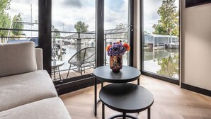 A modern room with a large window, a sofa, a small table, and a vase with flowers. - Luxury Watervilla Near Amsterdam and Schiphol (Aalsmeer)