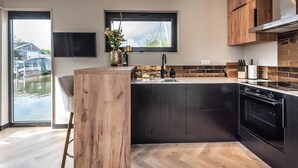 A modern kitchen with a large island, dark cabinetry, and a window overlooking a body of water. - Luxury Watervilla Near Amsterdam and Schiphol (Aalsmeer)