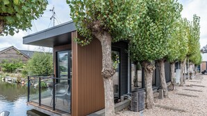 A modern house with a wooden deck overlooking a pond, a glass door, and a small outdoor seating area. - Luxury Watervilla Near Amsterdam and Schiphol (Aalsmeer)