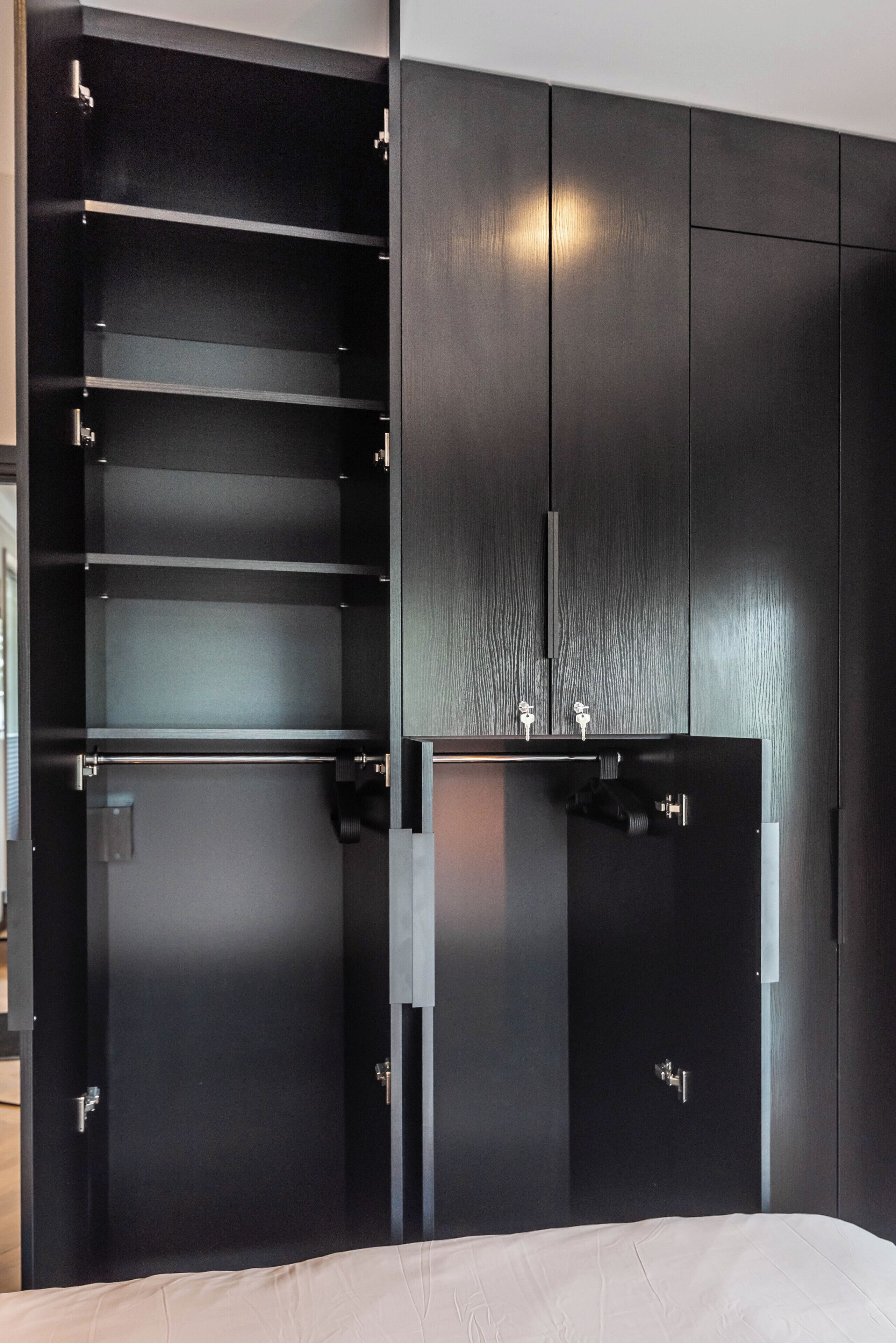 Et moderne soveværelse med en stor seng, indbygget garderobe med mange hylder og et lille natbord.