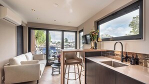 A modern kitchen with a large window, a built-in island with bar stools, and a flat-screen TV mounted above the island. - Luxury Watervilla Near Amsterdam and Schiphol (Aalsmeer)