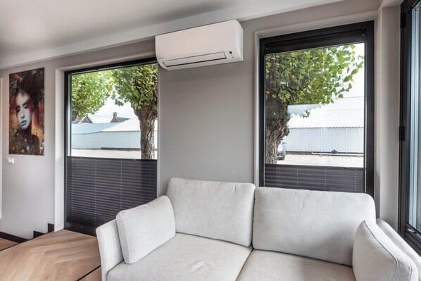 A modern living room with a sofa, large windows, and an air conditioning unit.