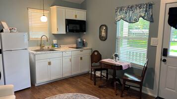 Una cocina con armarios blancos, un microondas negro, un lavamanos y una zona de comedor con mesa y sillas.