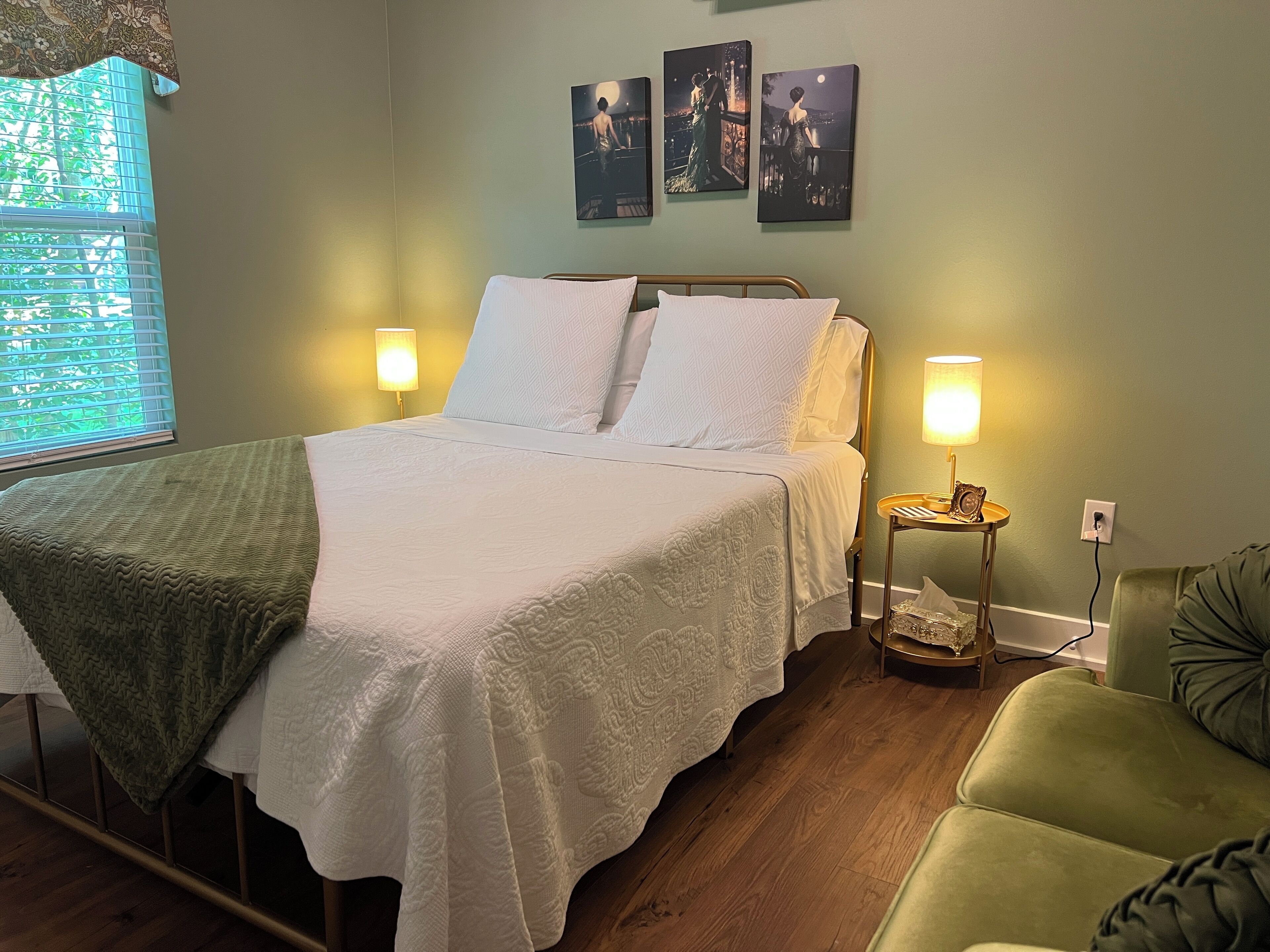 A neatly made bed with white linens, two bedside lamps, and a green armchair.