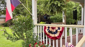 A porch with a Texas flag, a decorative wreath, and a hanging wind chime.