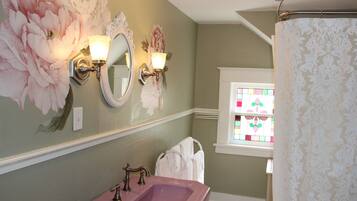 Une salle de bain avec un lavabo rose, un miroir agrémenté d’appliques murales et une fenêtre avec des vitraux.